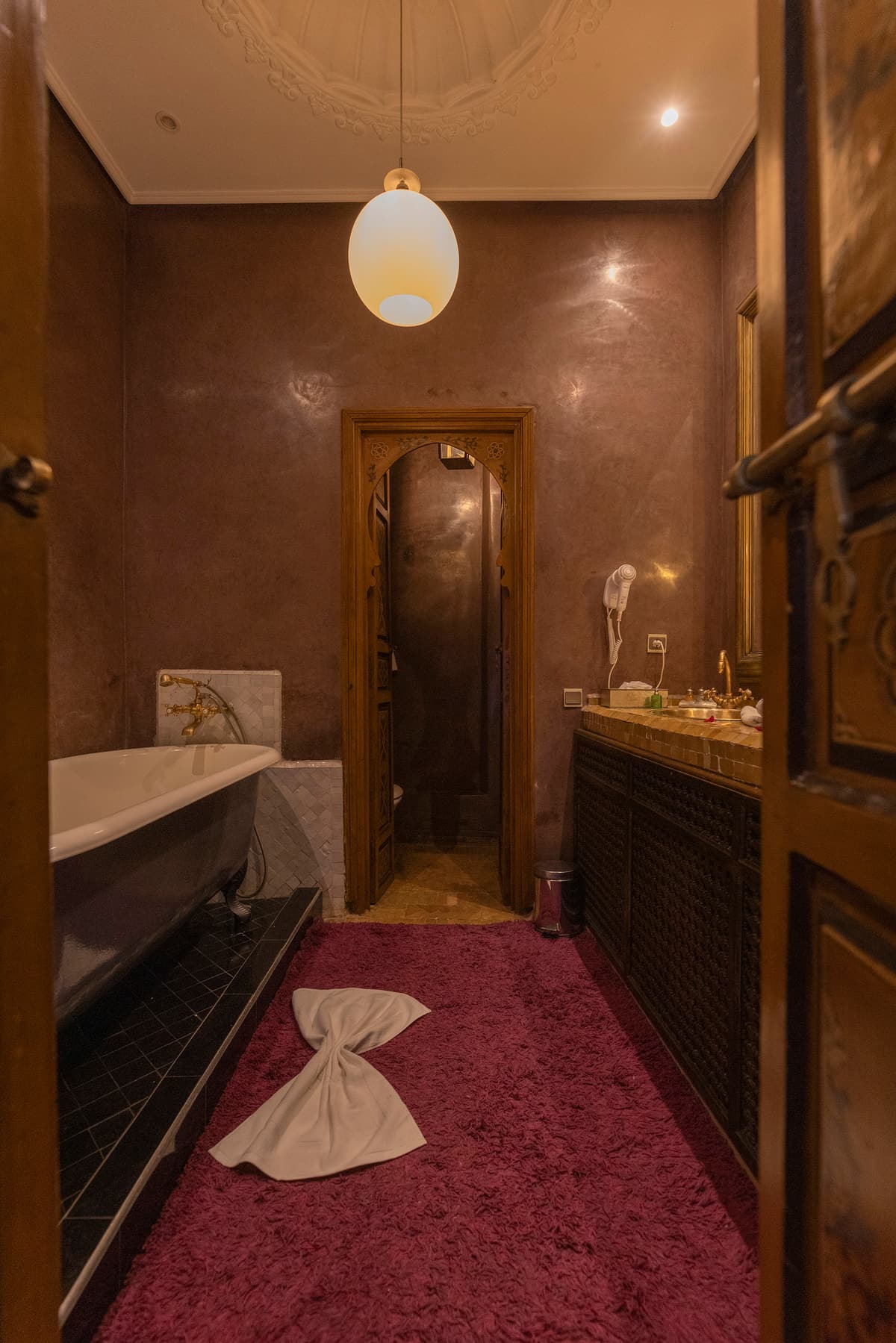 Salle de bains — baignoire sur pieds, tadelakt, robinetterie de laiton sous une rosace de plâtre sculpté