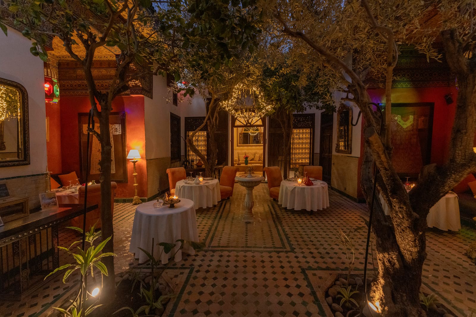 Un patio du riad la nuit, arcades éclairées de lanternes et reflets sur le zellige